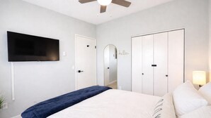 A bedroom with a bed, a TV mounted on the wall, a ceiling fan, and a wardrobe.