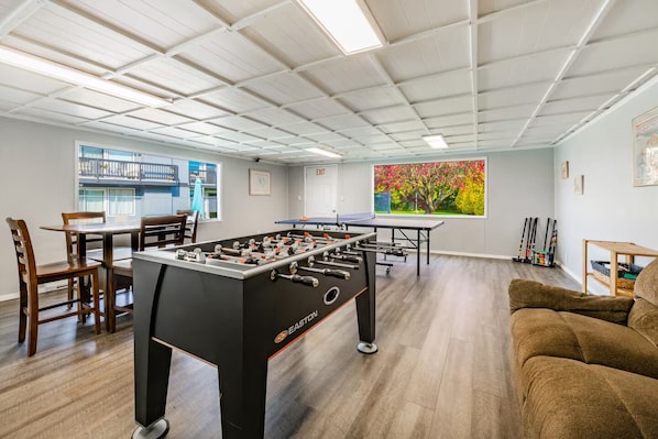 A room with a foosball table, a ping pong table, and a sofa.