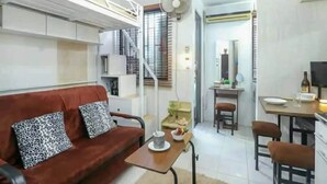 A compact living space with a sofa, a dining table, a fan, and a kitchen area. - One Metropolitan Place (Pasay)