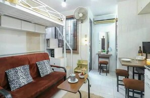 A compact living space with a sofa, a dining table, a fan, and a kitchen area. - One Metropolitan Place (Pasay)