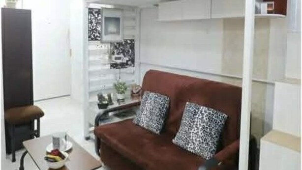 A compact living space with a sofa, a small table, a cabinet, and a bed. - One Metropolitan Place (Pasay)