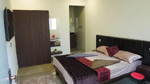 Ein Schlafzimmer mit Bett, Kleiderschrank, Fernseher und einem durchgehenden Türbogen einsehbarer Badezimmer.