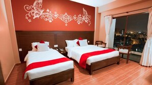 A hotel room with two beds, a large window with curtains, a city view, and a decorative wall design. - Hotel City Park Pokhara (Pokhara)