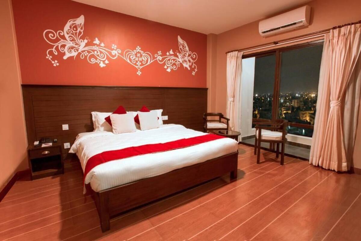 A hotel room with a large bed, a nightstand, a chair, and a view of the city at night.