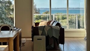 A room with a view of the sea, a sofa with a blanket, a small table, and a chair. - On the beach, Cowes, Phillip Island, Sleeps (Cowes)