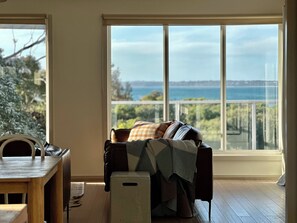 A room with a view of the sea, a sofa with a blanket, a small table, and a chair. - On the beach, Cowes, Phillip Island, Sleeps (Cowes)