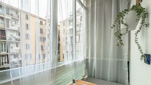 Ein Zimmer mit Blick auf Gebäude, ein Tisch mit zwei Gläsern, eine kleine Pflanze und ein Vorhang.