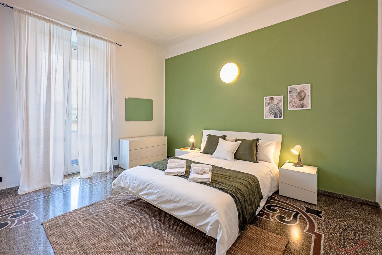 Una camera d'albergo con un letto, comodini, una parete verde e opere d'arte.