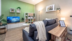 Ein modernes Wohnzimmer mit Sofa, Fernseher, Bücherregal und Zimmerpflanzen.
