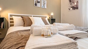 Ein ordentlich bezogenes Bett mit weißer und brauner Bettwäsche, ein Nachttisch mit Lampe und eine Wand mit gerahmten Kunstwerken.