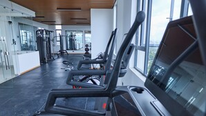 Academia equipada com esteiras, máquinas de musculação e uma grande janela.