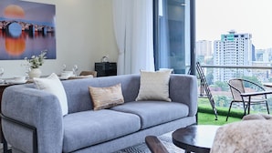 Uma sala de estar moderna com um sofá cinzento, um tapete estampado, uma mesa de jantar e vista para a cidade através de grandes janelas.