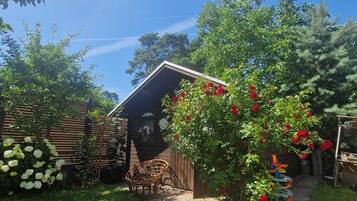 A wooden cabin with a sloped roof, surrounded by lush greenery and flowering plants.