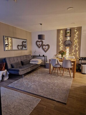 En moderne stue med en grå sofa, et spisebord med stole, et sofabord og dekorative billeder på væggen.