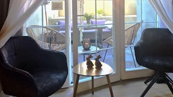 A room with two black chairs, a small round table, and a view through a glass door to an outdoor seating area with wicker furniture.