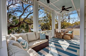 Eine überdachte Veranda mit einer Couch, Korbmöbeln und einem Deckenventilator.