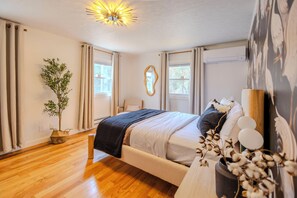 Ein Schlafzimmer mit einem Bett, einer Pflanze, einem Spiegel und einem Fenster.