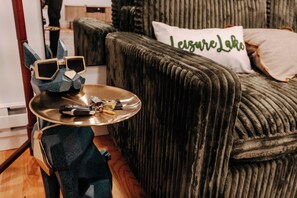 Ein üppiges Sofa mit einem Kissen mit der Aufschrift 'LeisureLake', ein kleiner Tisch mit einer Ablage für Sonnenbrille und Autoschlüssel sowie ein Sessel mit einem blauen Kissen.