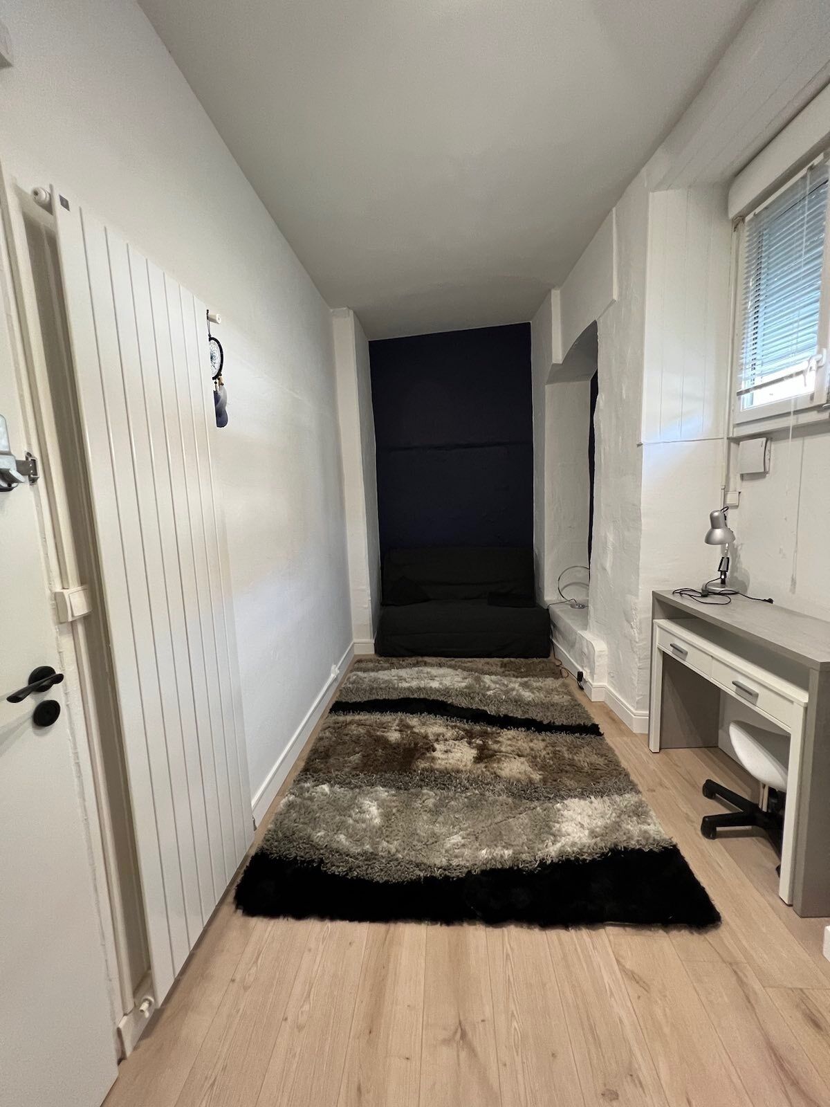 A hallway with a white door, a desk with a lamp, and a dark wall.