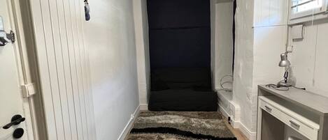 A hallway with a white door, a desk with a lamp, and a dark wall.