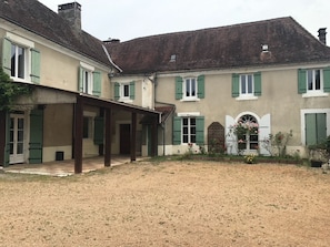 A two-story building with a covered patio area, a gravel courtyard, and a garden with flowers.
