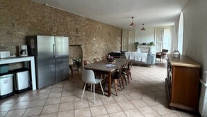 Een ruime keuken met een stenen muur, een eethoek met tafel en stoelen, en een grote koelkast.