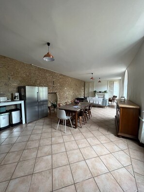 A spacious kitchen with a stone wall, a dining area with a table and chairs, and a large refrigerator.