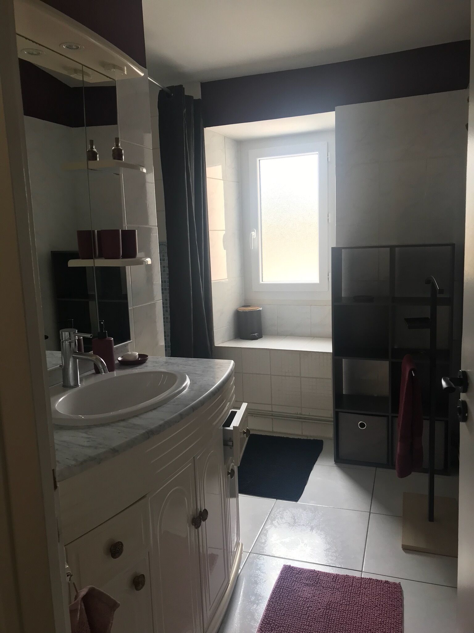 Un bany modern amb un mirall gran, un lavabo, una finestra i un moble d'emmagatzematge negre.