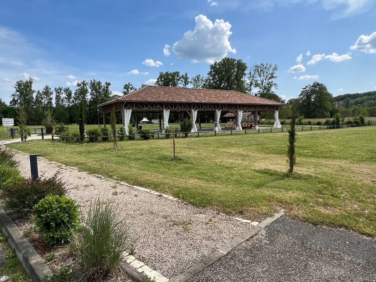 Een paviljoen met een pannendak, omgeven door een grindpad en gras.