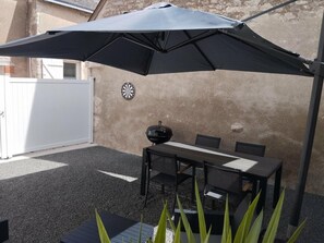 Eine Terrasse im Freien mit Tisch, Stühlen, einem Grill und einem Dartspiel.