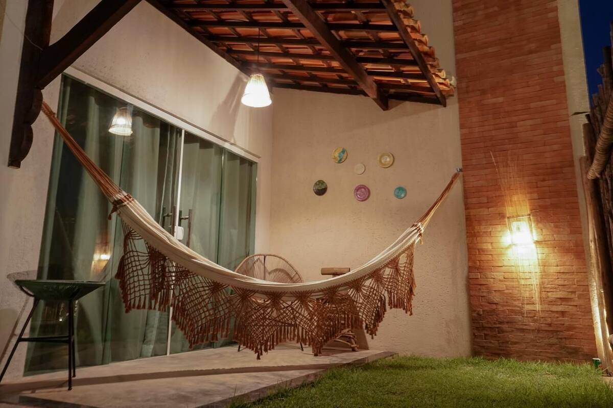Un hamac sous une pergola en bois, une porte vitrée et un mur décoré d’assiettes.