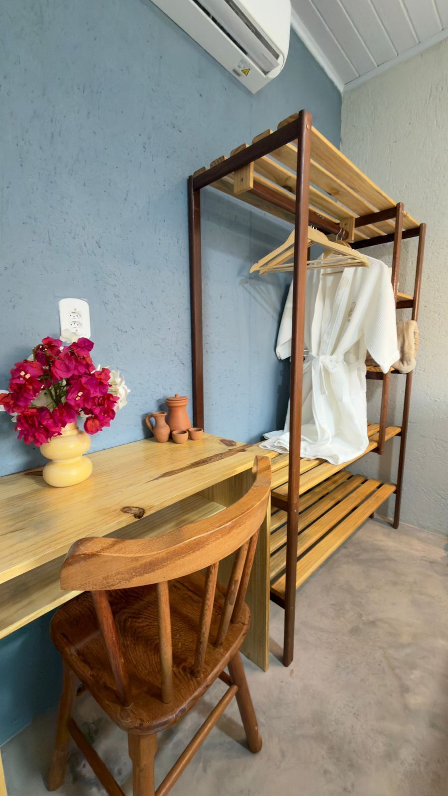 Una cama litera con un escritorio y silla de madera, un jarrón de flores y un aire acondicionado instalado en la pared.