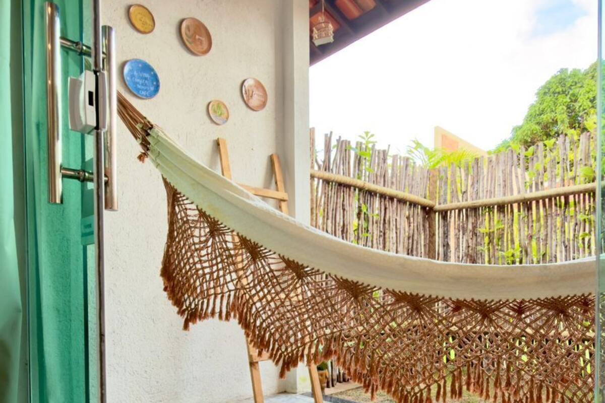 Un hamac suspendu au-dessus d’un sol en béton, une clôture en bois et une porte dotée d’un cadre vert.