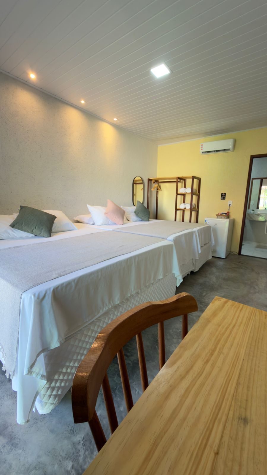 Ett hotellrum med två sängar, en trästol, ett bord och en luftkonditioneringsanläggning.