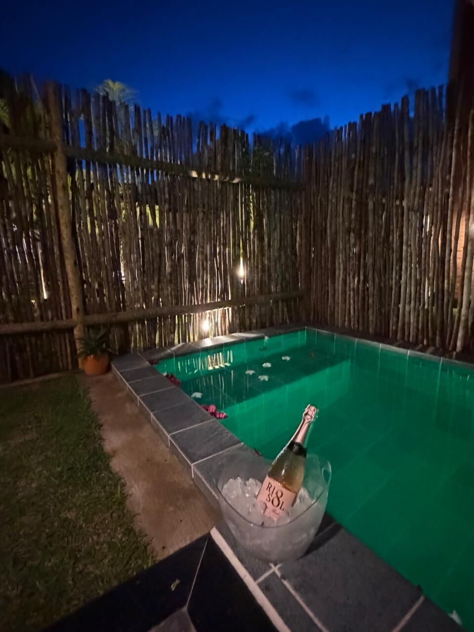 A swimming pool with a bottle of champagne in a bowl of ice, surrounded by a wooden fence.