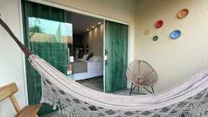 A hammock, a wicker chair, and a bed in a room with a green door and a wall with decorative plates. - Vila Gaheri (São Miguel dos Milagres)