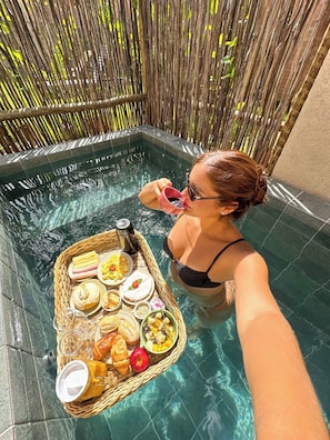 A person in a swimming pool with a tray of food and drinks.