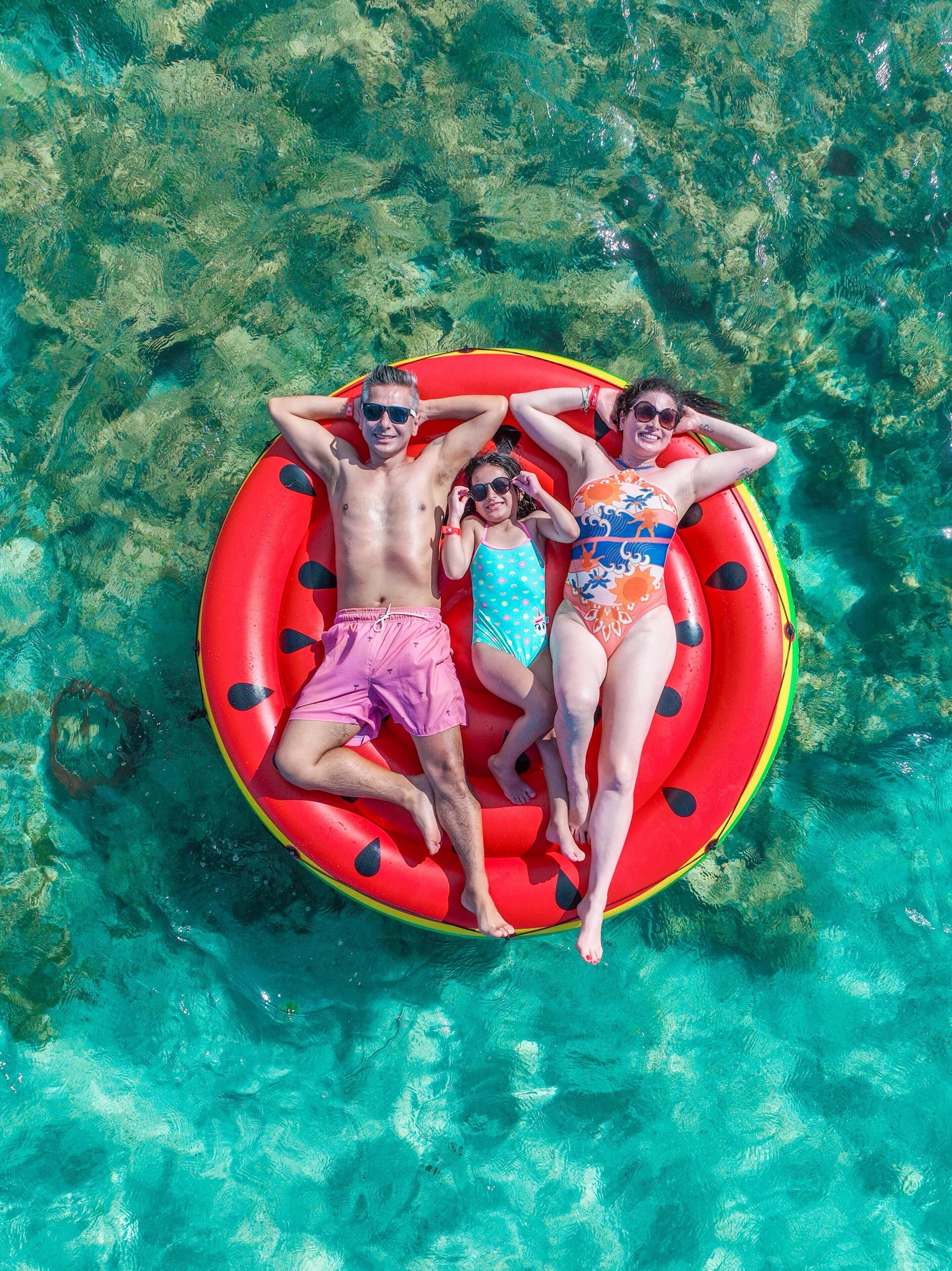 Tres personas en un flotador rojo en agua cristalina.