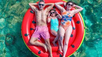 Tres personas en un flotador rojo en agua cristalina.