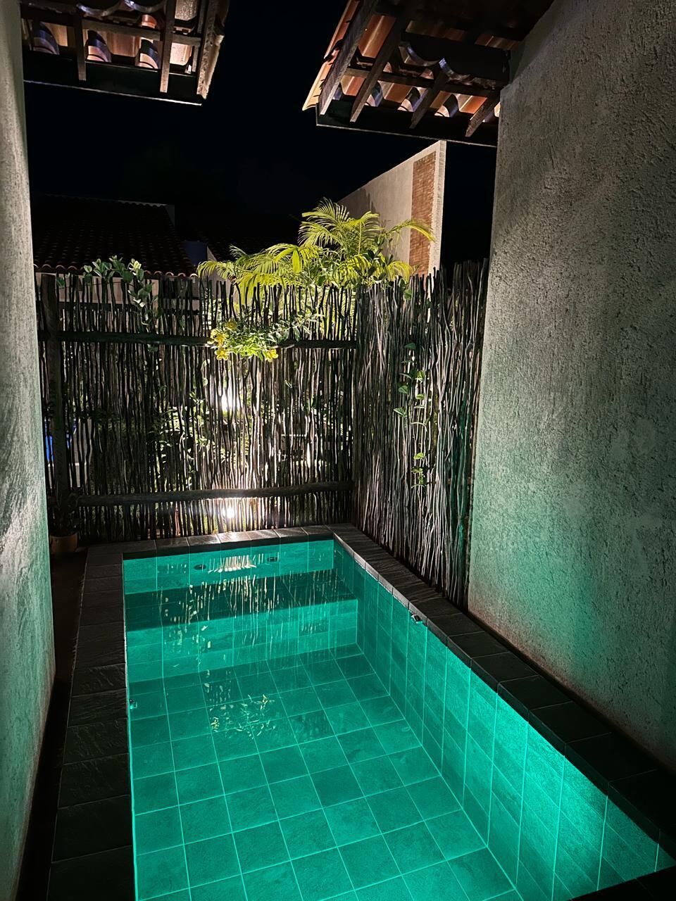 Una piscina con cerca de bambú y pared de hormigón.