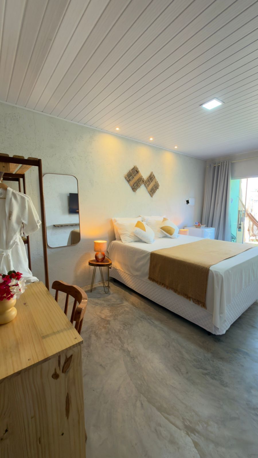Een slaapkamer met een bed, nachtkastje, lamp, spiegel en uitzicht.