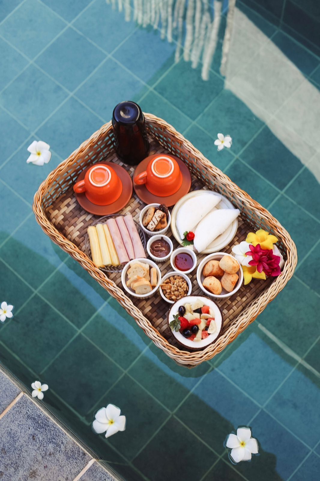 A wicker tray with various food items and a teapot on a poolside.