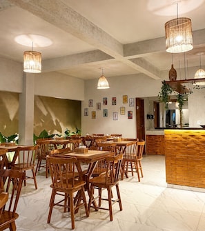 A spacious dining area with wooden tables and chairs, hanging pendant lights, and a brick accent wall.