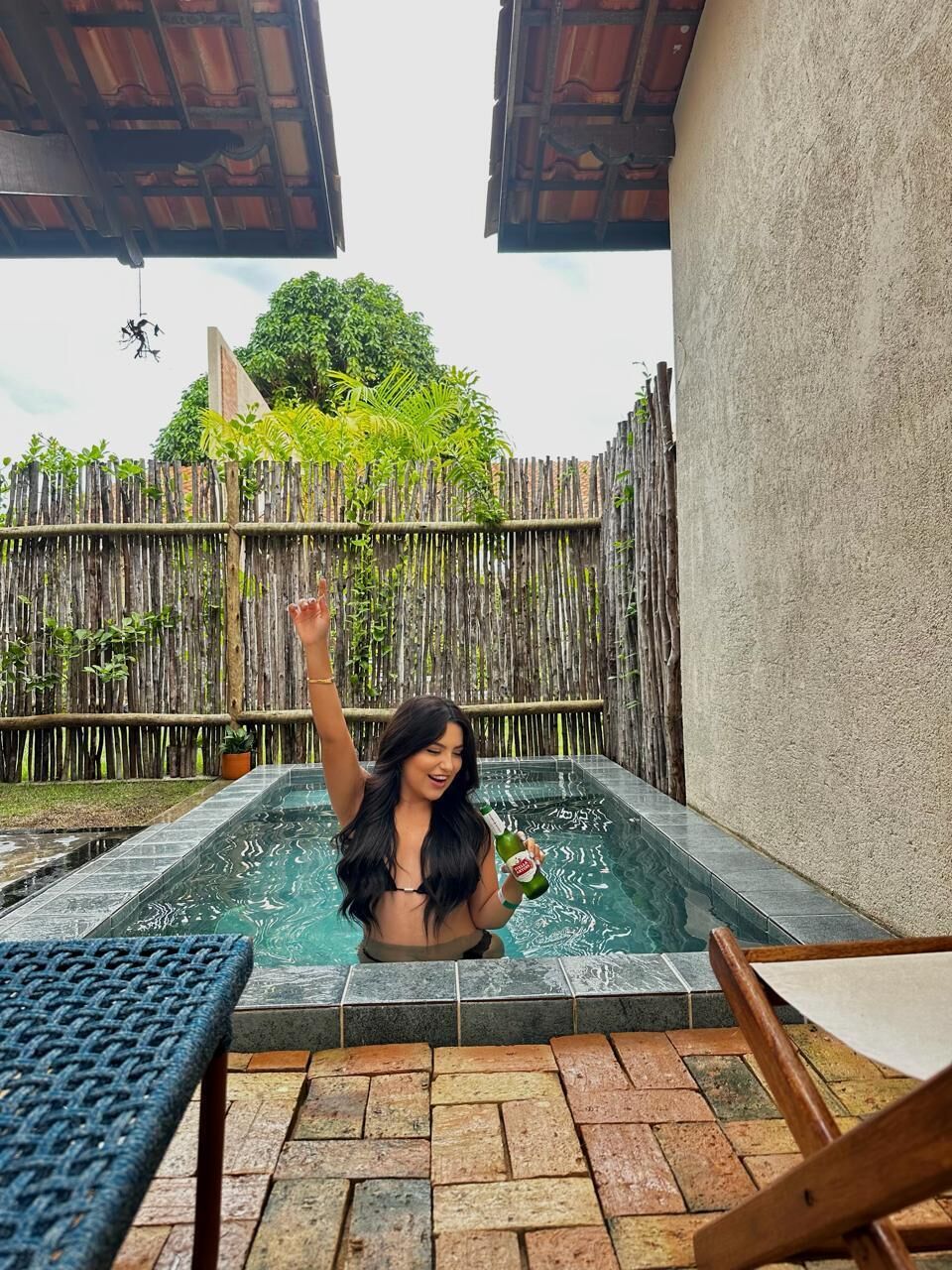 A person in a small outdoor pool with a bamboo fence and a wooden pergola in the background.