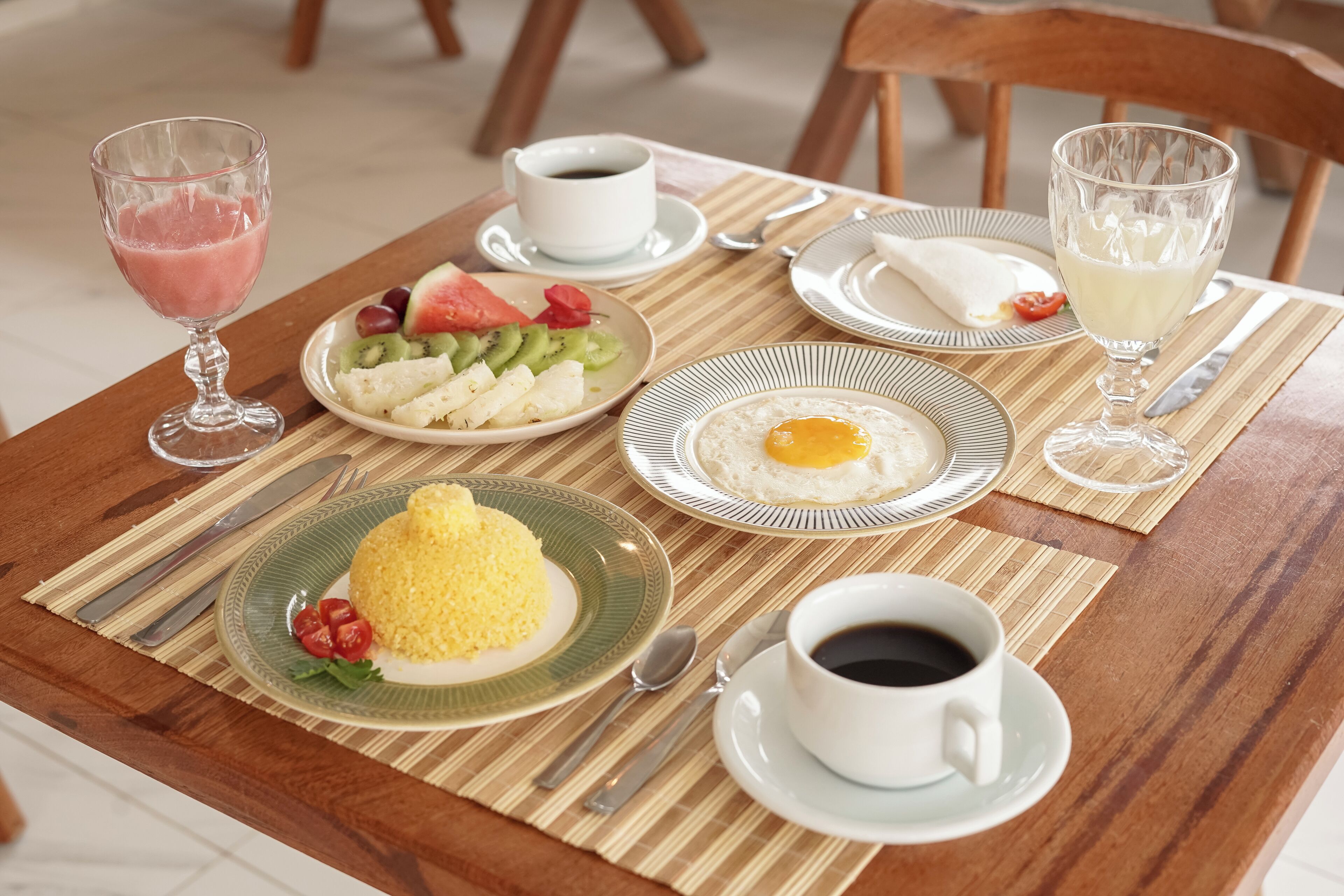 Una mesa de desayuno con platos de comida, un vaso de jugo y tazas de café.