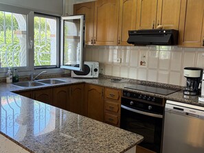 A kitchen with granite countertops, wooden cabinets, a built-in oven, a dishwasher, and a window with a view of greenery. - Villa with private pool and AC - 10 guests (Miami Playa)