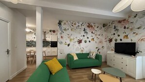 Una sala de estar moderna con un sofá verde, una mesita pequeña, un televisor de pantalla plana y un papel tapiz con motivos florales.