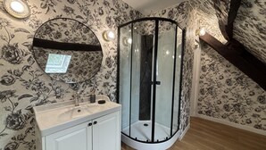 Un baño con tocador blanco, espejo redondo y cabina de ducha con mampara de vidrio.