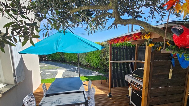 A patio with a table and chairs, a grill, and a blue umbrella. - Single-storey house with quiet garden - 6 guests (Royan)
