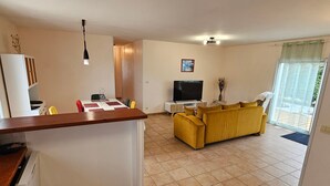 A living room with a yellow sofa, a TV, and a dining area with a table and chairs. - Single-storey house with quiet garden - 6 guests (Royan)